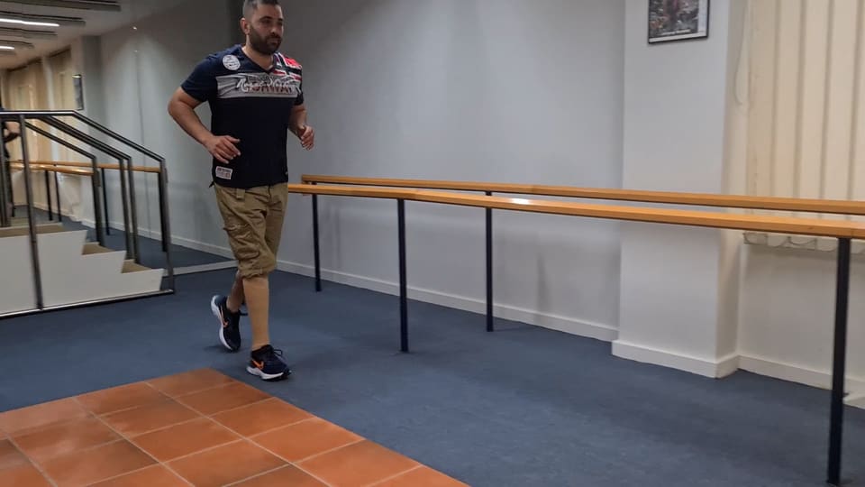 A patient with a prosthetic leg walking in the workshop's gait training area after amputation