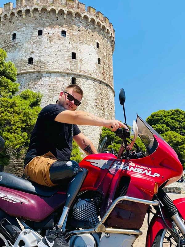 Above-knee prosthesis user with a C-Leg knee on a motorbike in front of the White Tower, Thessaloniki